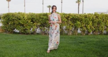 Uzun yaz elbiseli, çiçekli bir kadın yaz parkında yürüyor. 