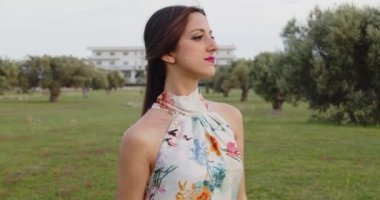 Uzun yaz elbiseli, çiçekli bir kadın yaz parkında yürüyor. 