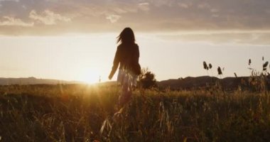 Beyaz şortlu, siyah deri ceketli gün batımında yaz tarlasında yürüyen genç bir kız.