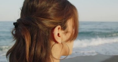 Siyah çizmeleri ve beyaz pantolonu olan güzel bir İtalyan kızı yazın denizde yürüyor.