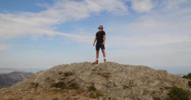 Spor elbiseli bir adam gündüz vakti kayanın üstünde duruyor. 