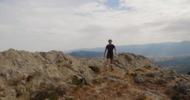 Spor elbiseli bir adam gündüz vakti kayanın üstünde duruyor. 