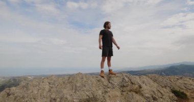 Spor elbiseli bir adam gündüz vakti kayanın üstünde duruyor. 