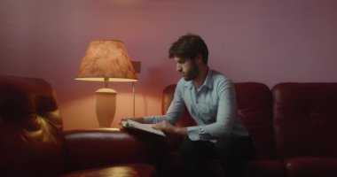 Yakışıklı genç adam kanepede oturup kitap okuyor.