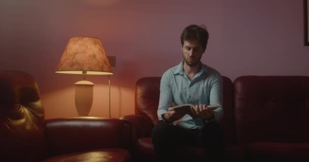 Handsome Young Man Reading Book While Sitting Sofa Home — Stock Video