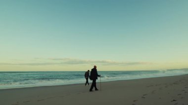 Fırtınalı okyanus dalgalarının yanında, iki adam rahatça yürüyor..