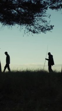 Sabahın köründe denize yakın ağaçların arasında yürüyen iki kişinin silueti..