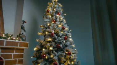 Şöminenin yanındaki karla kaplı Noel ağacında kurdeleli hediyeler var..