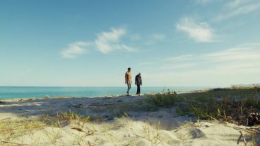 Okyanusa yakın güneşli bir sahilde iki insan rahatlamak için yürür..