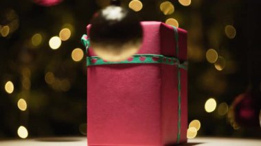 Küçük kırmızı Noel hediyesi ağacın önünde ve sallanan topların arasında dönüyor..