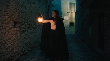 Gizemli genç kadın pelerin ve fenerle bir köyün sokaklarında yürüyor..