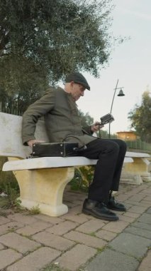 Yaşlı adam antika film kamerasını meydanda bir bankta kuruyor.