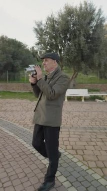 Yaşlı adam süper 8 kamerasıyla parkta video çekiyor.