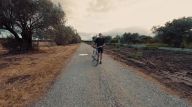 Bir adam bisikletiyle doğal bir parkta yürür..