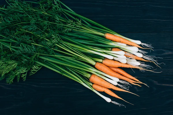 Молодая морковь и лук на черном фоне — стоковое фото
