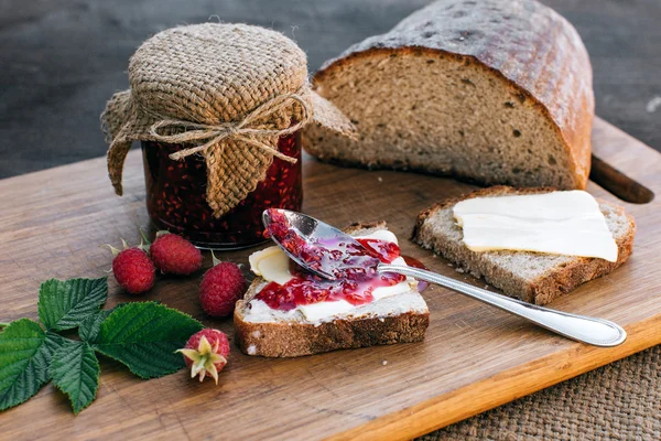 Selai raspberry dan roti dengan mentega dalam guci di atas meja kayu Makan siang sarapan Stok Foto