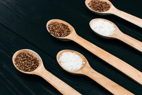 Riso e semole di grano saraceno nel cucchiaio di legno sul tavolo nero — Foto Stock
