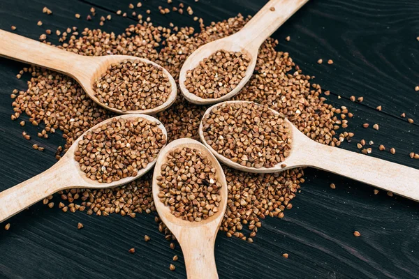 Semole di grano saraceno e cucchiaio di legno sul tavolo nero — Foto Stock