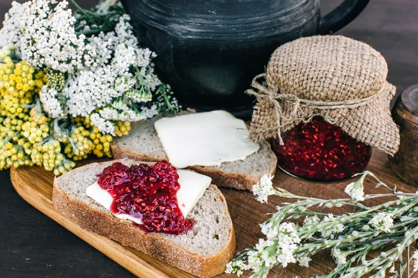 Marmellata di lamponi e pane con burro in un barattolo e tisana calda sul tavolo di legno Colazione a pranzo — Foto Stock