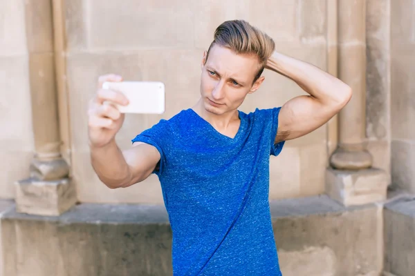 Ung flot mand med kort hår tager en selfie i en urban kontekst på mobil - Stock-foto