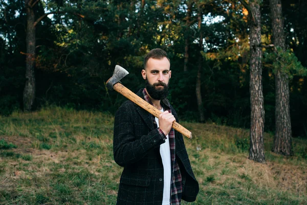 Retrato brutal barbudo hipster hombre en el bosque con hacha —  Fotos de Stock