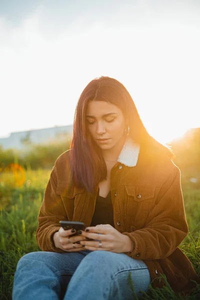 Teenager Pomocí Svého Telefonu Zatímco Sedí Zelené Louce Během Západu — Stock fotografie