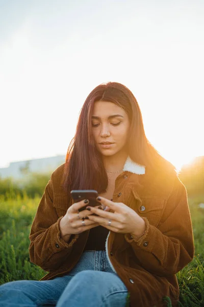 Teenager Drží Svůj Telefon Zatímco Sedí Zelené Louce Během Západu — Stock fotografie