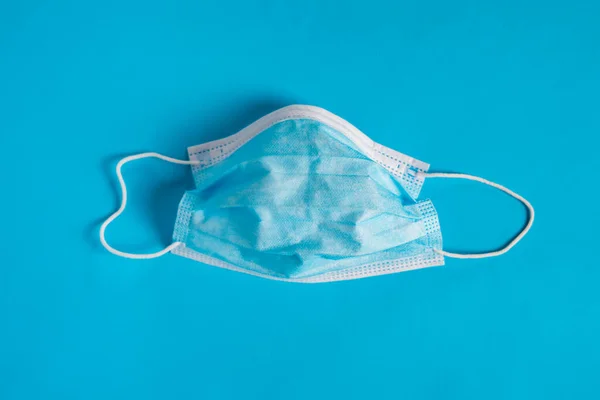 An used surgical face mask isolated on blue background. Corona-virus protection.