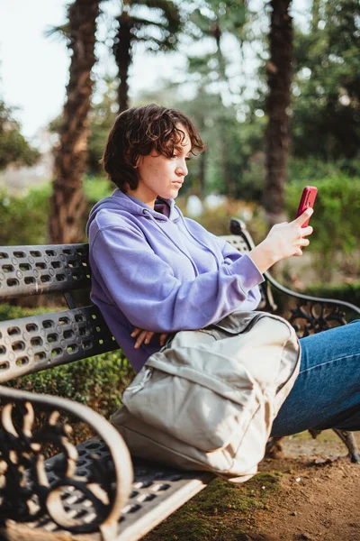 Dívka Sedí Lavičce Parku Dívá Svůj Mobilní Telefon — Stock fotografie