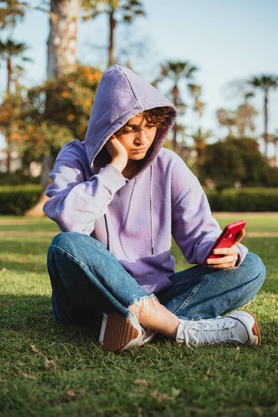 Nudný Teenager Purpurové Mikině Používá Mobilní Telefon Parku Sedí Trávě — Stock fotografie