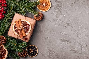 Noel kompozisyonu. Hediye kutusu, tarçın, anason, kurutulmuş meyve, kozalak ve gri arka planda köknar iğneleri. Üst görünüm kopyalama alanı