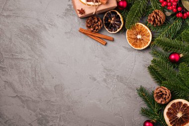 Noel kompozisyonu. Hediye kutusu, toplar, tarçın, anason, kurutulmuş meyve, kozalak ve gri arka planda köknar iğneleri. Üst görünüm kopyalama alanı