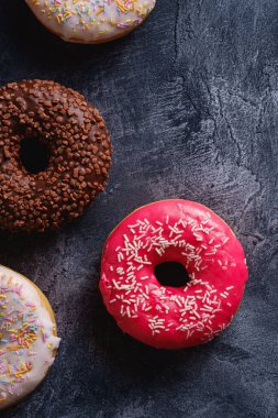 Çikolata, pembe ve vanilyalı çörekler serpiştirilmiş tatlı yiyecekler koyu beton desenli arka plan, üst manzara