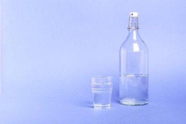 Mavi arka planda, şişenin yanındaki su bardağı.