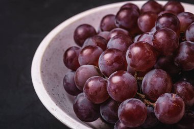 Taze üzümler beyaz ahşap kasede koyu taş arka planda, açı açılı makro.
