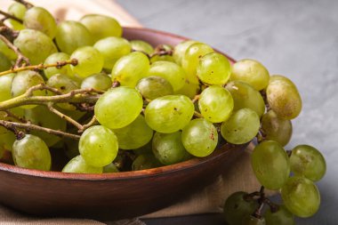 Tahta kasede, keten masa örtüsünün üzerinde taze, olgun, beyaz üzüm üzümleri, taş beton arka plan, açı görünümü.
