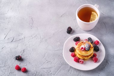 Süzme peynirli krep ve pudra şekeri, kremalı börek ahududu ve böğürtlenli tatlı limon dilimli sıcak çay bardağının yanında.