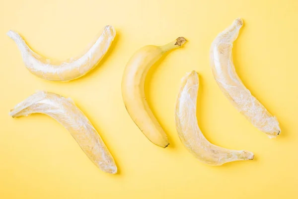 Banana fruits wrapped in stretch plastic on yellow background