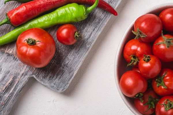 Eski ahşap kesim tahtasının yanında taze olgun domatesler sıcak kırmızı biberli, beyaz taş beton arka plan, üst manzara.