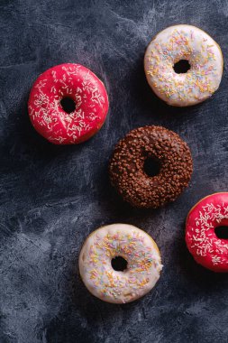 Çikolata, pembe ve vanilyalı çörekler serpiştirilmiş tatlı yiyecekler koyu beton desenli arka plan, üst manzara