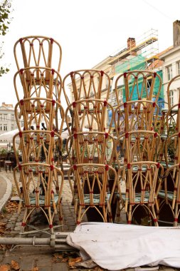 Tarihi binaların yakınındaki kentsel bir alanda hasır kafe sandalyeler yığılmış. Kavramsal şehir fotoğrafı sezon tatilini veya restoran tatilini simgeliyor..