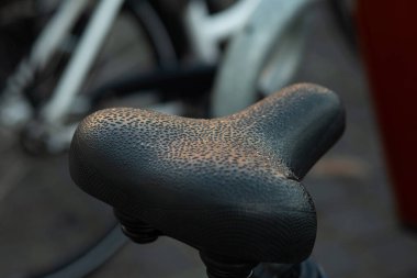 Sıcak güneş ışığıyla kaplı ıslak bir bisiklet koltuğunun yakın çekimi. Doğal dokusu ve yansıması olan kentsel detay kavramı.