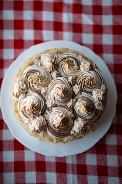 Kırmızı kareli masa örtüsü üzerine krema süslemeli ev yapımı pastanın üst görünümü.