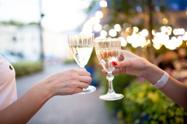 Akşam ışıklarında şampanya bardaklarını tokuşturan iki kişi.