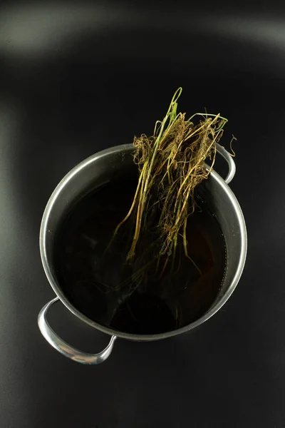 Bitki kökleri içeren koyu sıvı bir metal kap. Uzun süre depolandıktan sonra doğal kuruma ve yaşlanma belirtilerini gösteriyor..