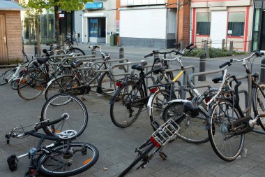 Şehir ortamında halka açık bir bisiklet parkında birden fazla bisiklet sıralanmış. Görüntü günlük şehir hareketliliğini ve halka açık alanlarda bisiklet sürmenin varlığını gösteriyor..