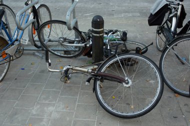 Halka açık park alanlarının yanındaki metal bir direğin yanında duran bisikletlerin yakın görüntüsü. Sahne, şehirdeki günlük hareketlilik ve bisiklet varlığını yansıtıyor..