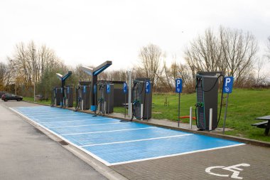 Bulutlu bir günde birden fazla hızlı şarj ünitesi ve işaretli park yeri olan modern elektrikli araç şarj istasyonu. Sürdürülebilir ulaşım altyapısı ve temiz enerji teknolojisi.