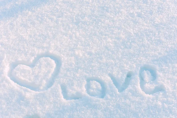 Hand-painted heart and word love on snow in sunny winter day. Concept of Valentines day, romantic celebration, winter wedding