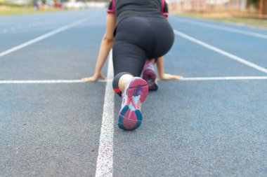 Koşan kadın stadyumdaki mavi pistte poz veriyor.